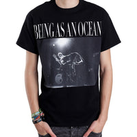 image of a white man with his hands in pants pockets wearing a black tee shirt on a white background. tee has full chest print in white that says being as an ocean at the top, with a photograph of two guys in the band playing guitar
