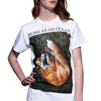 image of a woman from the neck down with her hand on her hip wearing a white tee shirt on a white background. tee has full body print that says in black on top, being as an ocean with a photo of a sleeping fox on green grass.