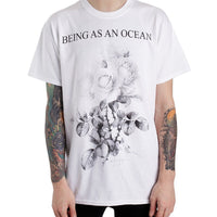 image of a man from the neck down with tattoos on each arm wearing a white tee shirt on a white background. tee has full body print in black that says at the top, being as an ocean, with roses below