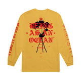 image of the back of a gold long sleeve tee shirt on a white background. the long sleeve  has a full back print of black roses and the words being as an ocean over the roses in red
