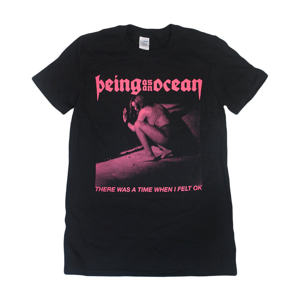 image of a black tee shirt on a white background. tee has a full chest print in pink. at the top says being as an ocean, below is a woman crouched down with her hand up looking behind her shoulder and the words there as a time when I felt OK written along the bottom