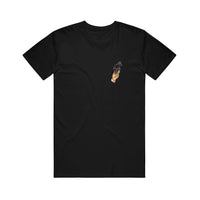 image of a black tee shirt on a white background. the tee has a small print on the right chest of a tan hand holding a blue and red bird tied up in rope.