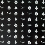 close up image of a square sheet of holiday wrapping paper. paper is black, with white christmas trees, ornaments and the words being as an ocean alternating throughout, filling the paper. 