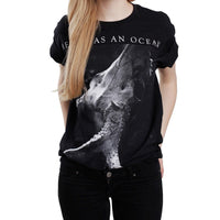image of a white woman with blonde hair from the neck down wearing a black tee shirt on a white background. tee has a full body print that has at the top in white being as an ocean with a black and white photo of a deer skull with antlers below.