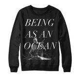 image of a black crewneck sweatshirt on a white background. crewneck has full body print in white that says being as an ocean, over a black and white photo of a man in a striped shirt playing guitar.