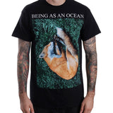 image of  man from the neck down with tattoos on each arm wearing a black tee shirt on a white background. tee has full body print that says in white on top, being as an ocean with a photo of a sleeping fox on green grass.